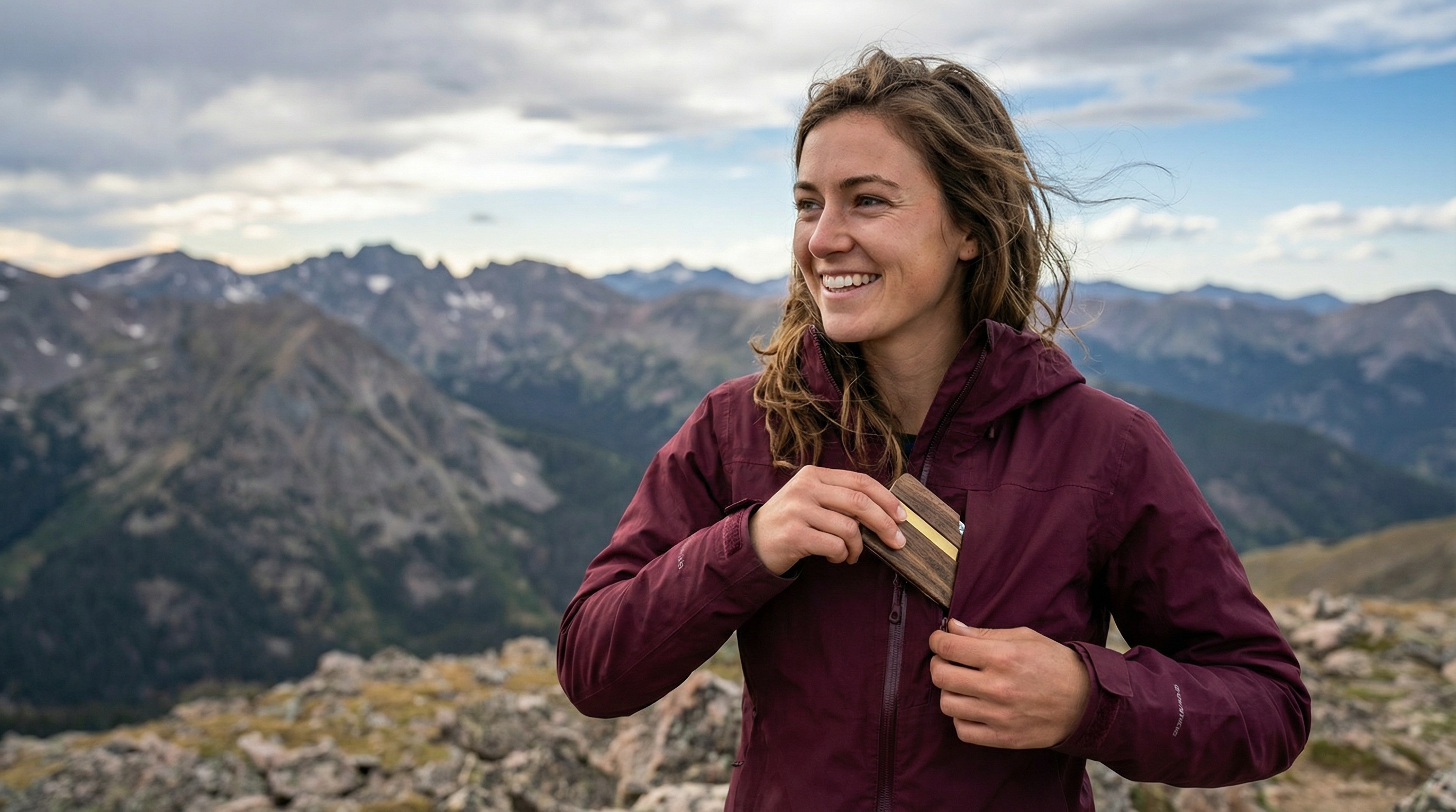 Female hiker at Colorado mountain summit pulling out Tomi Wallet from jacket pocket